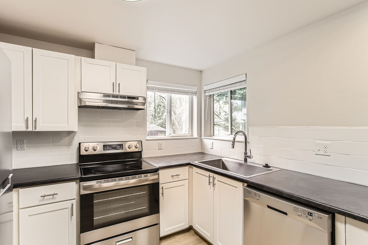 Modern kitchen with sleek stainless steel appliances, white cabinetry, and large windows for natural light.