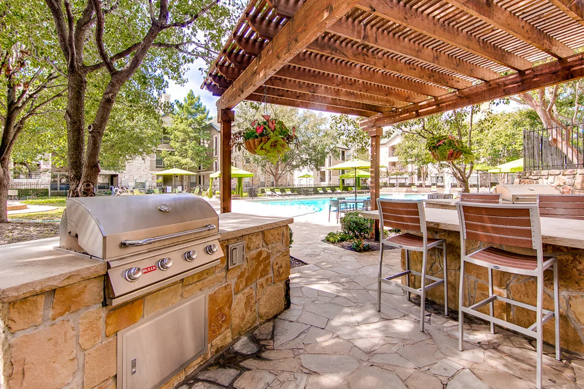 Inviting outdoor patio with grill under a stylish pergola, overlooking a pristine swimming pool and lush, green landscape.