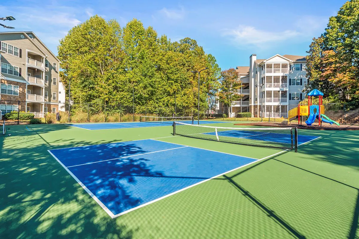 Modern apartment complex with vibrant tennis court and colorful playground, surrounded by lush greenery.