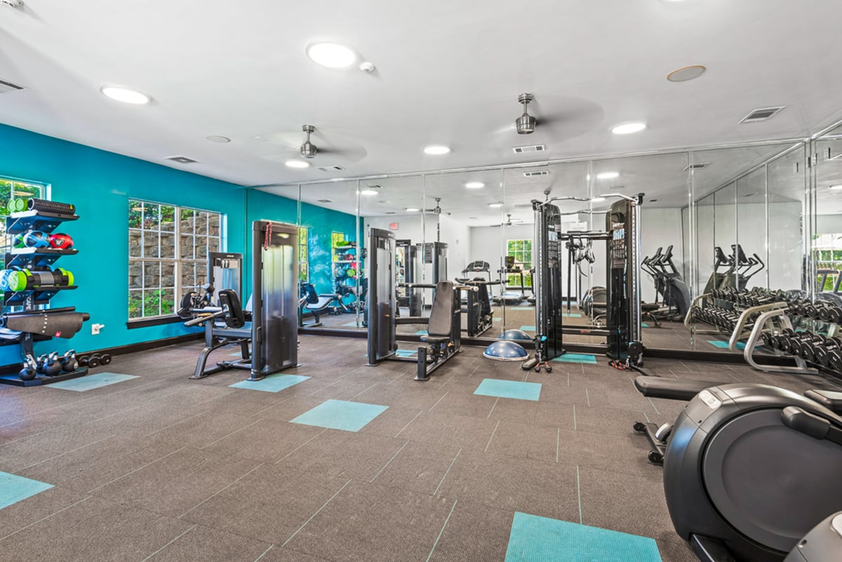 Modern fitness center with state-of-the-art equipment, vibrant teal accents, and ample natural light.