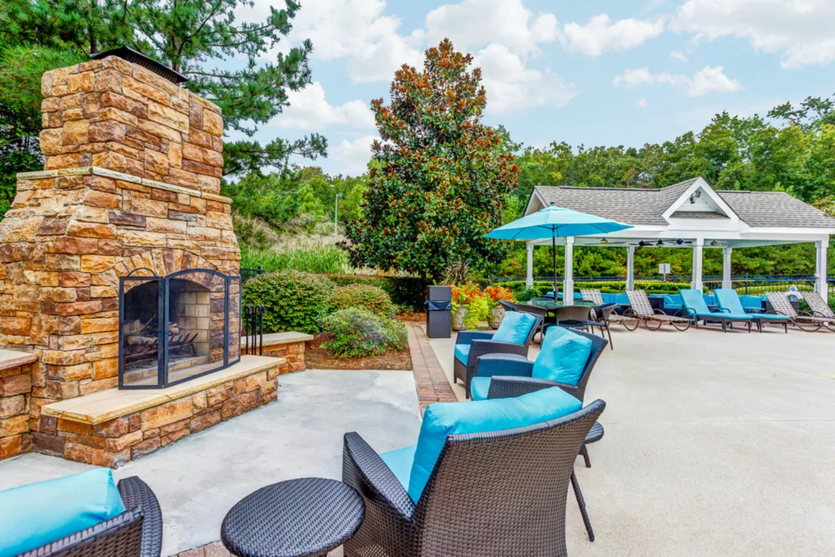 Inviting outdoor space featuring a rustic stone fireplace, comfortable wicker seating with vibrant blue cushions, and a shaded pergola for relaxation.