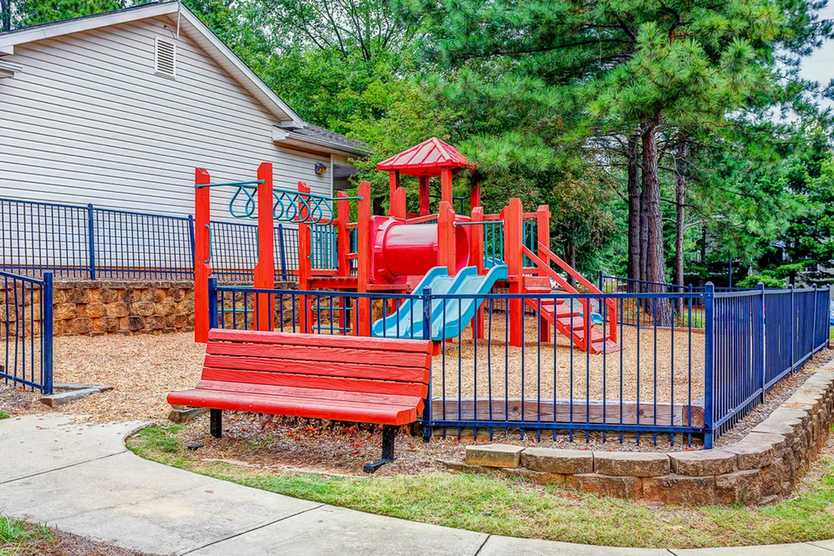 Charming playground with vibrant red and blue equipment surrounded by lush trees, perfect for children’s outdoor fun.