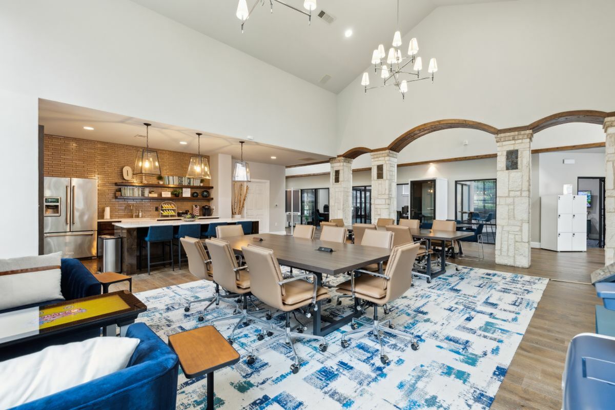 Elegant co-working space featuring a modern communal table with plush chairs, a sleek kitchen with stainless steel appliances, and stylish lighting fixtures set against a high-ceilinged interior with stone archways.