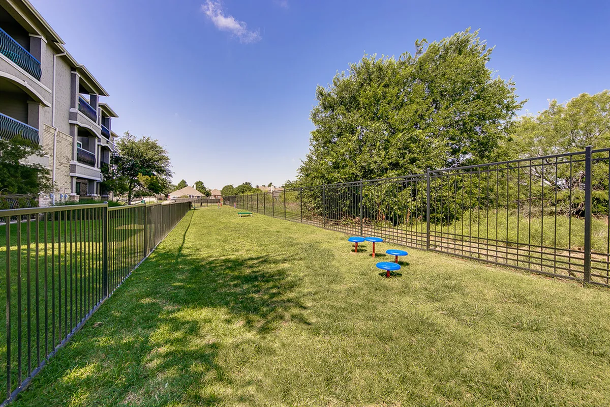 Inviting outdoor green space featuring a fenced grassy area with vibrant blue play structures, perfect for relaxation and recreation.