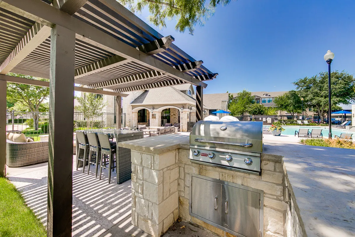 Charming outdoor area with a modern grill station, stylish pergola, and inviting seating, perfect for entertaining near a sparkling pool.