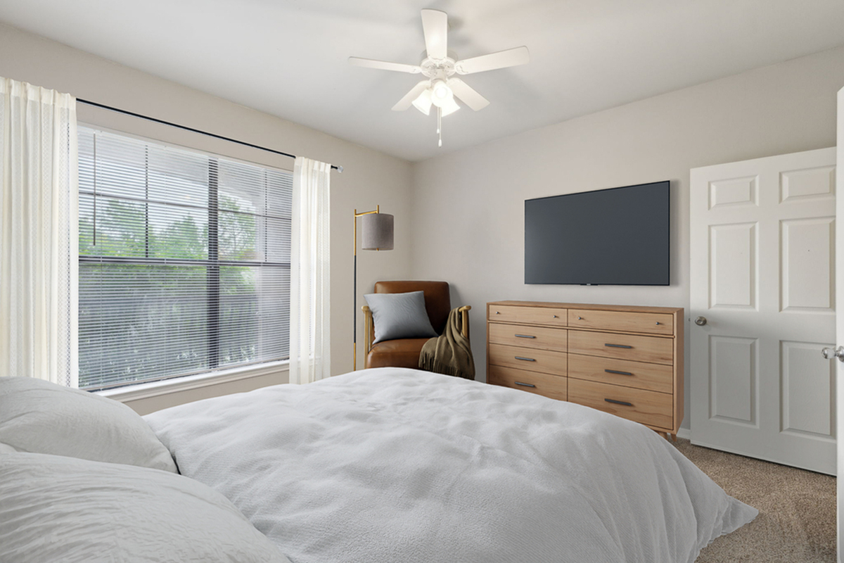 Bright and inviting bedroom with cozy bedding, stylish dresser, and natural light pouring through large windows.