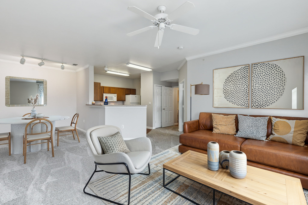 Modern open-concept living room with a brown leather sofa, cozy armchair, and stylish kitchen in background, perfect for entertaining.