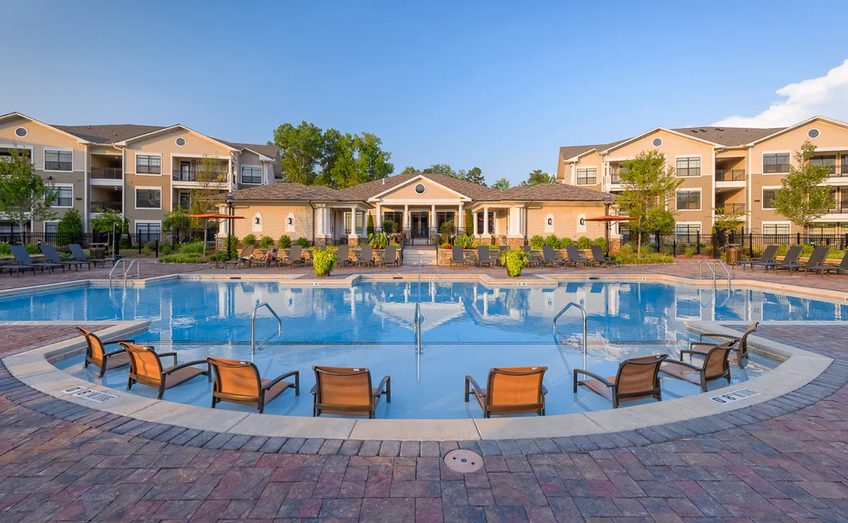 Luxurious apartment complex with a stunning, expansive swimming pool, stylish poolside seating, and beautifully landscaped surroundings.