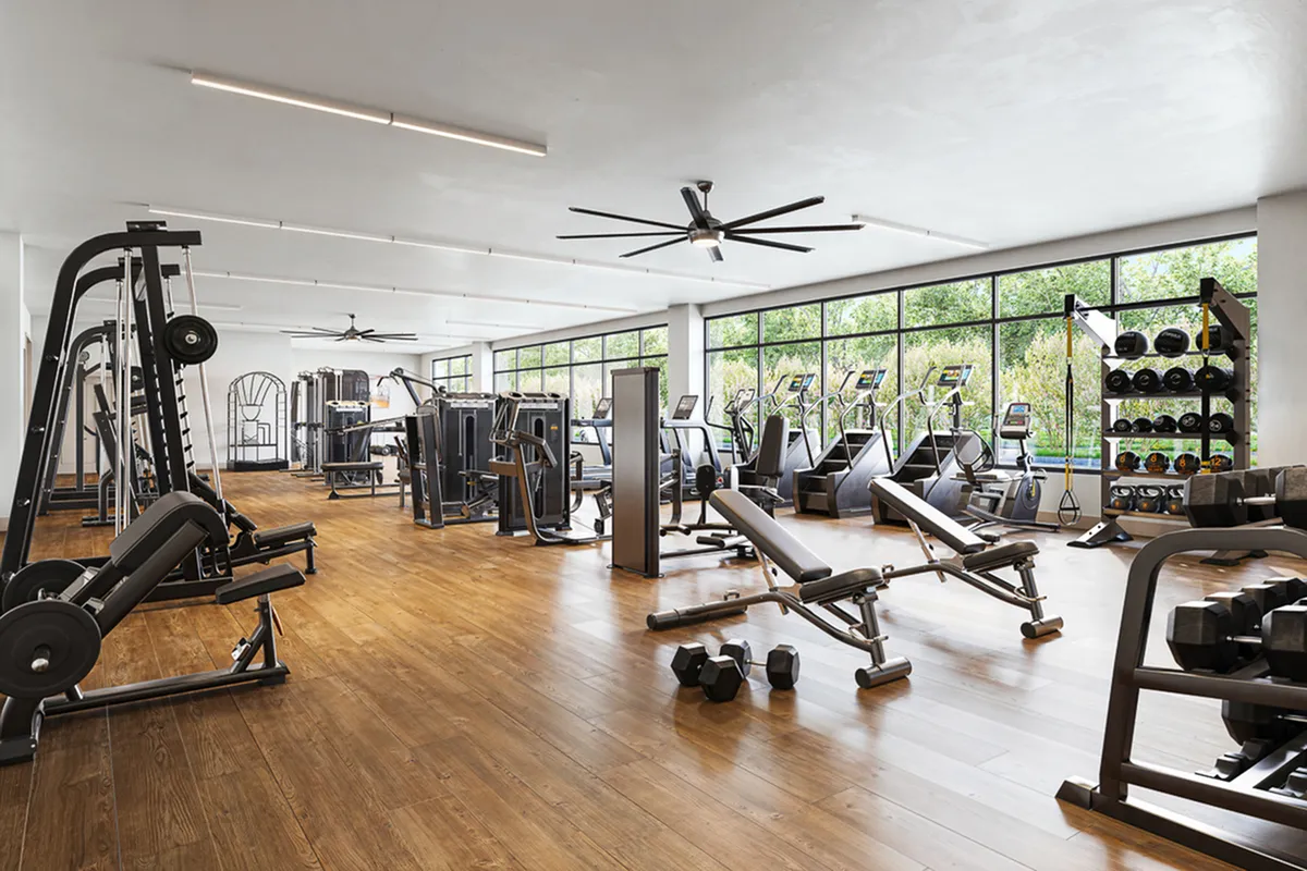 Spacious, modern fitness center with top-of-the-line equipment, bright natural lighting, and sleek wooden floors.