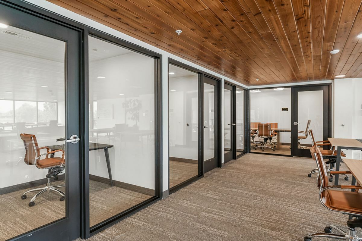 Modern office space featuring glass-walled meeting rooms with stylish wooden ceilings and sleek office chairs.