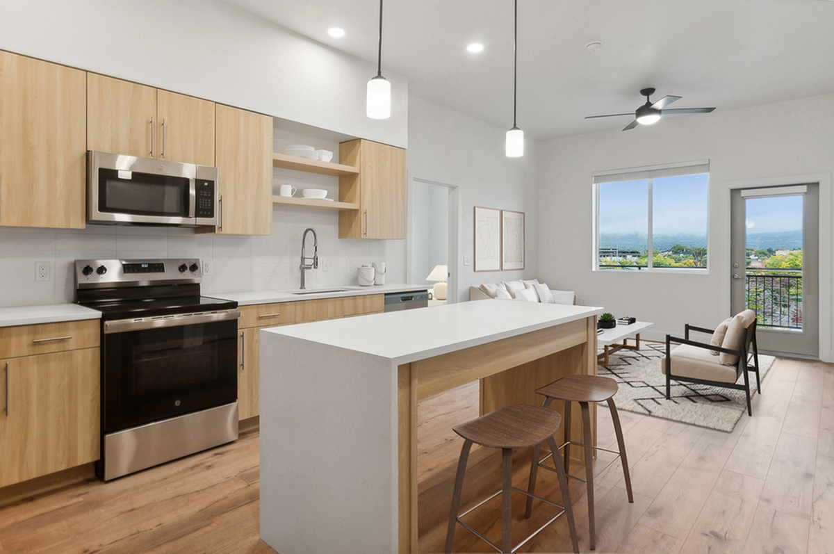 Modern open-concept kitchen and living room with sleek wooden cabinetry, stainless steel appliances, and a large window overlooking scenic views.