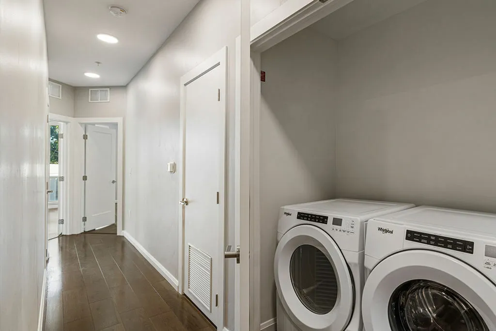 Modern apartment hallway with sleek hardwood floors, featuring an efficient laundry area with a washer and dryer at Sugarmont Apartments