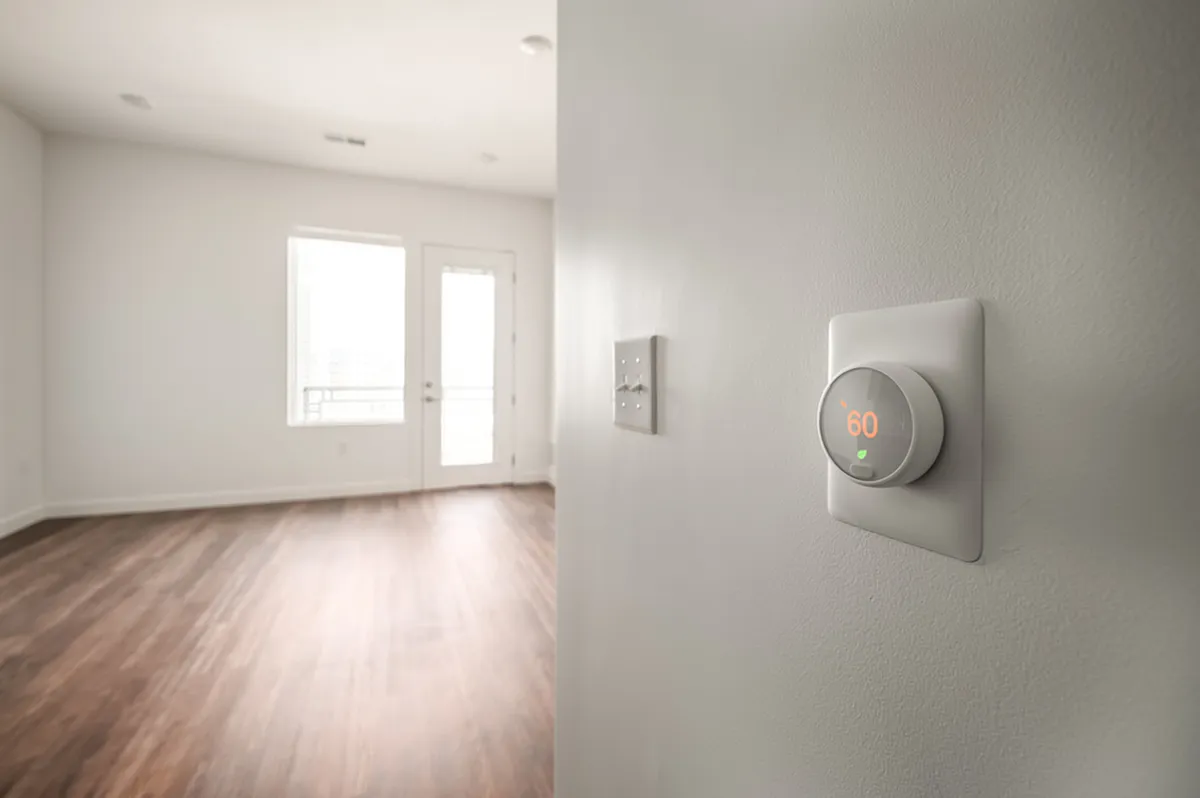 Modern apartment with smart thermostat, featuring elegant wood flooring and abundant natural light through large windows.
