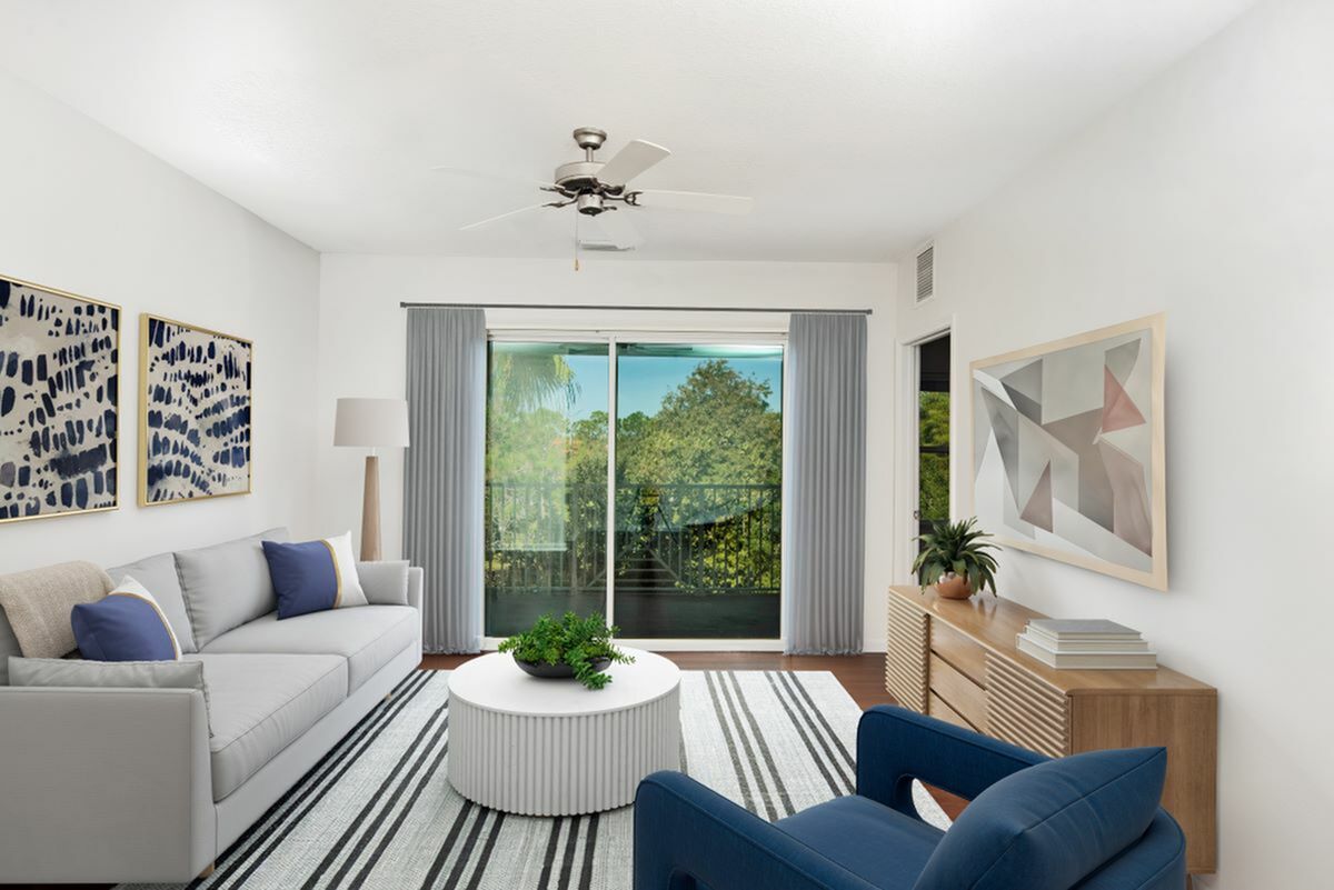 Bright, modern living room with elegant decor, featuring a grey sofa, vibrant artwork, and large windows showcasing a lush green view.