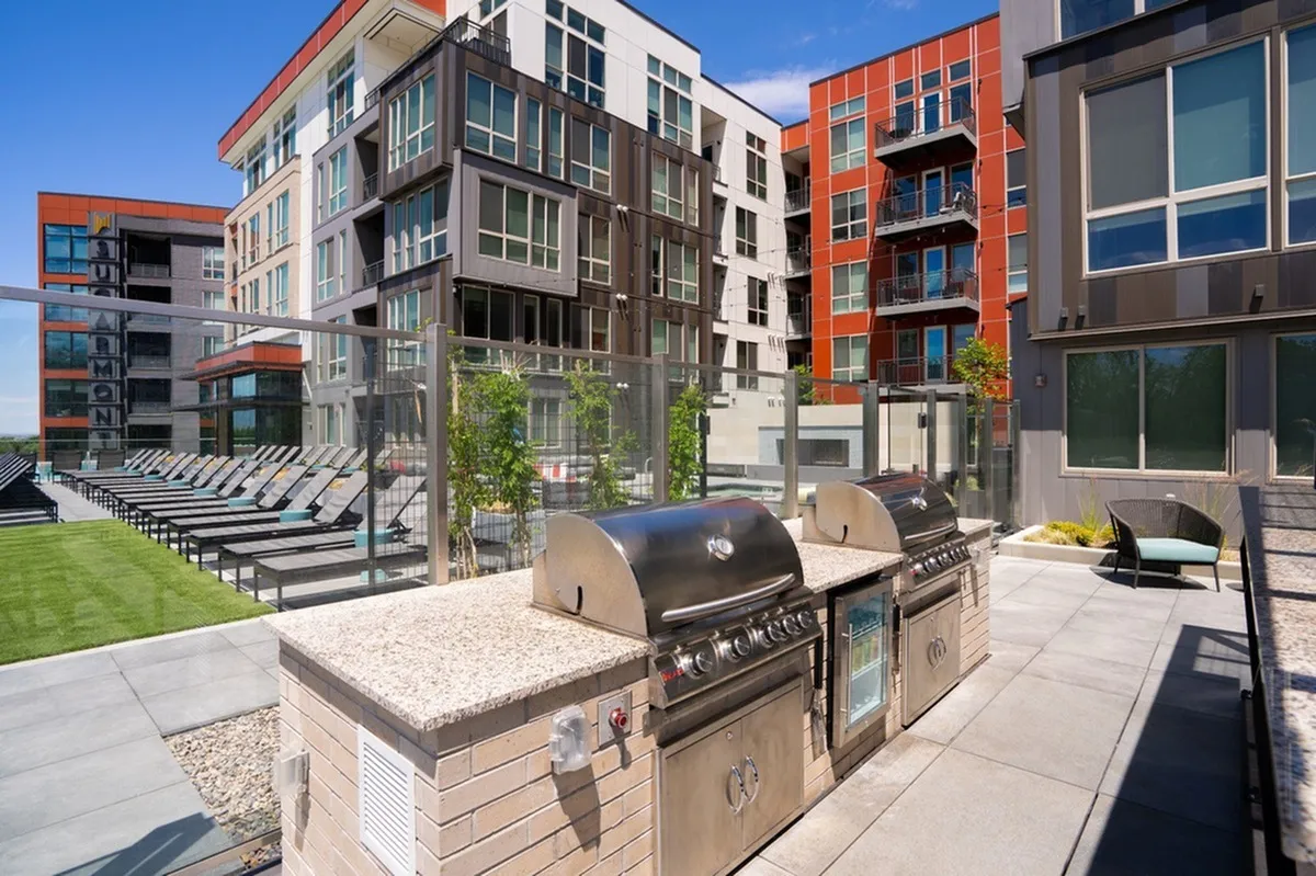 Modern apartment complex with vibrant outdoor decks, featuring a stylish outdoor barbecue area and sunlit lounging space with outdoor grills