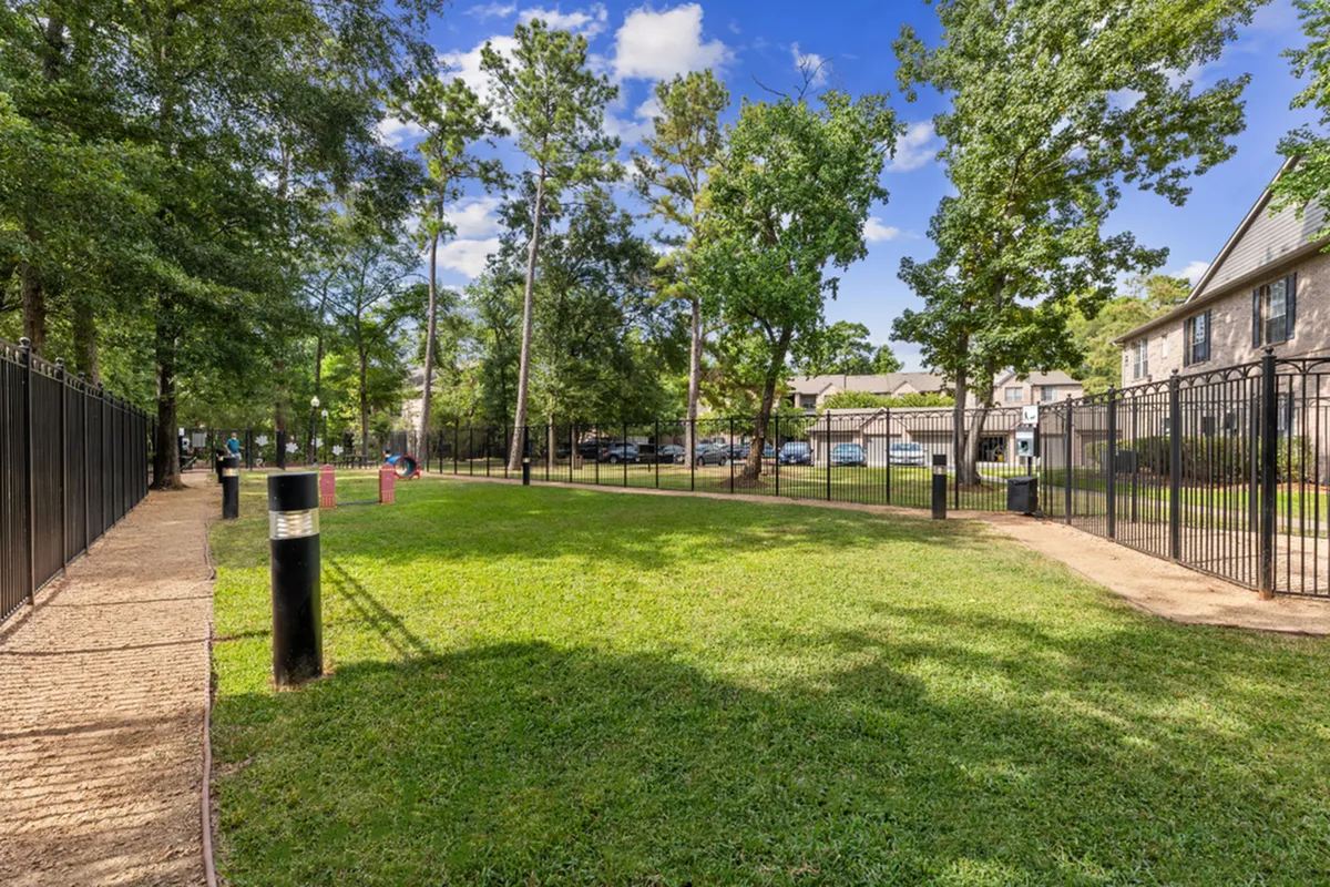 Lush, pet-friendly park with well-kept grassy area and black metal fencing, perfect for outdoor enjoyment in a serene apartment community setting at Raveneaux Apartments in Houston Texas