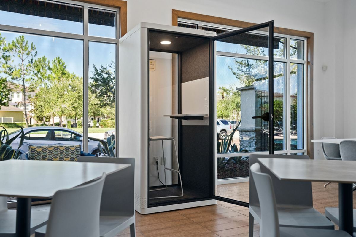 Modern coworking space with a sleek privacy pod and stylish furniture under natural light from large windows at Apt CoWork at The Marq highland Park in Westchase Tampa