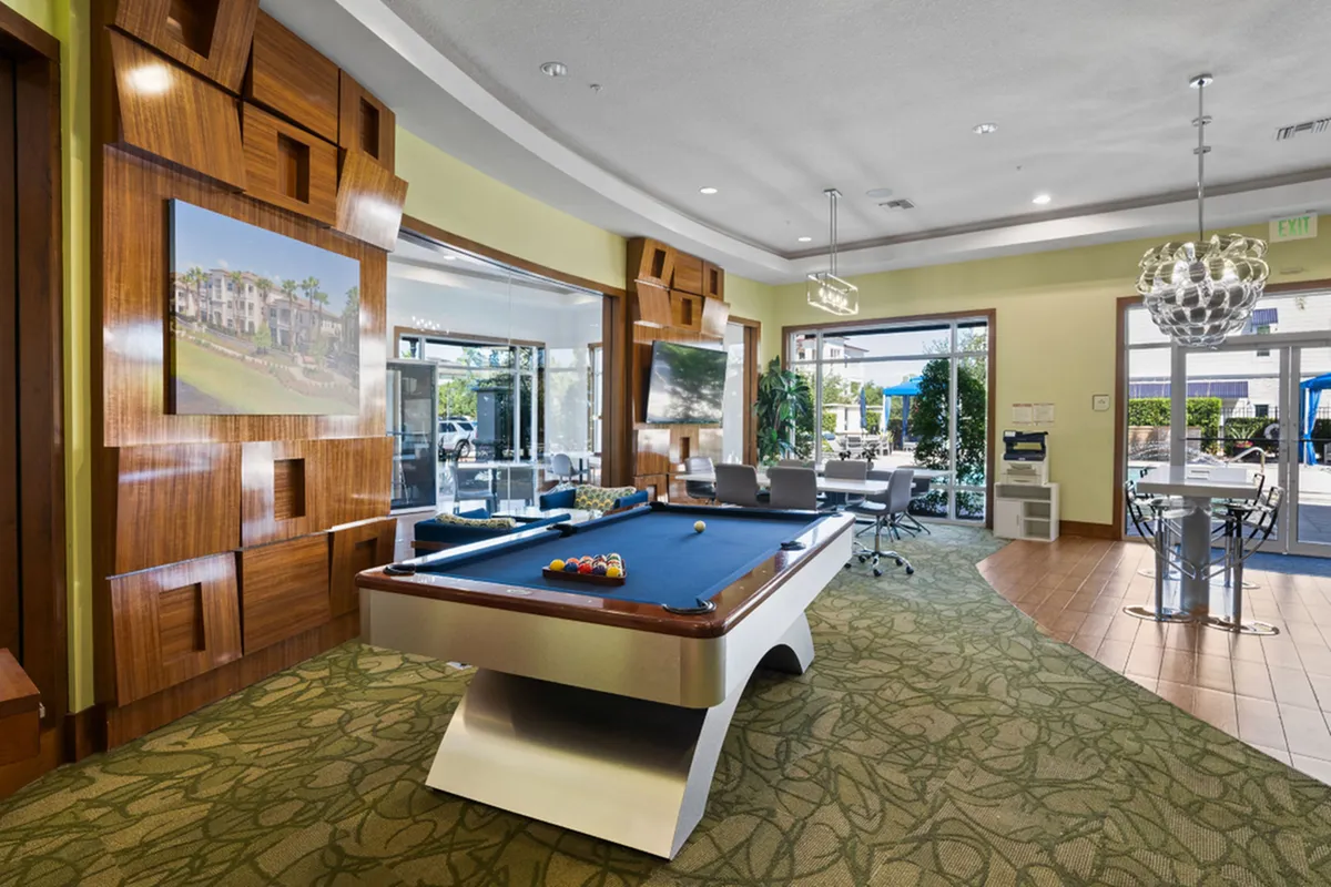 Luxurious recreation room with a sleek pool table, modern wood accents, and ample natural light, perfect for entertaining and relaxation at The Marq Highland Park Apartments in Westchase Tampa, Florida