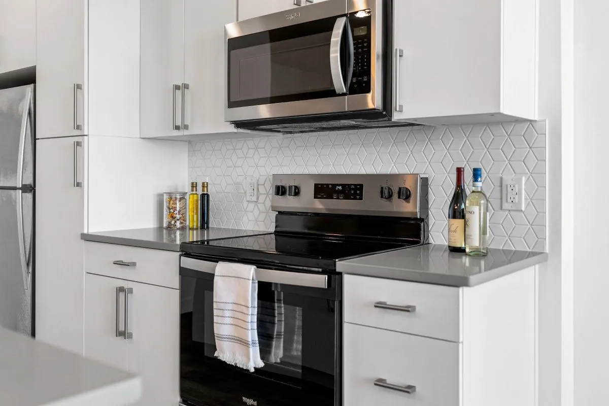 Modern kitchen with sleek stainless steel appliances, elegant white cabinetry, and geometric tile backsplash at The Richmond Apartments