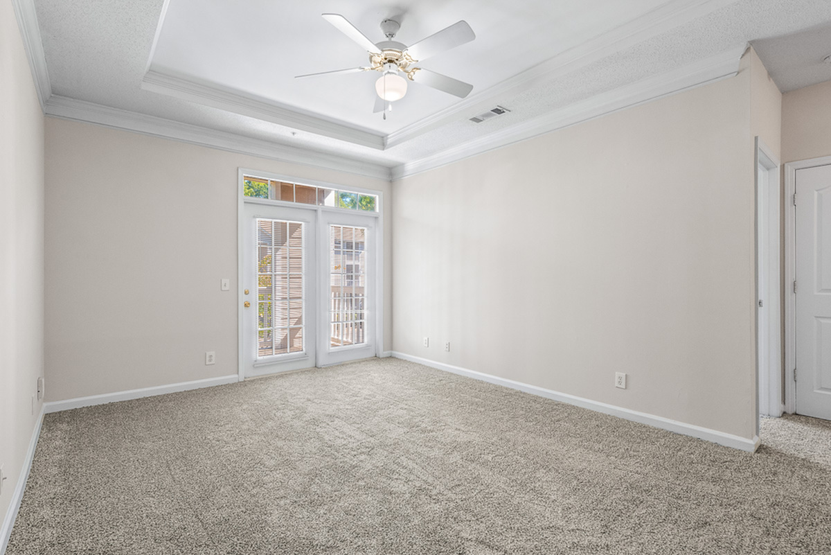 Bright, inviting room with plush carpet, high ceiling, and elegant French doors leading to a balcony at Retreat at Peachtree City Apartments.
