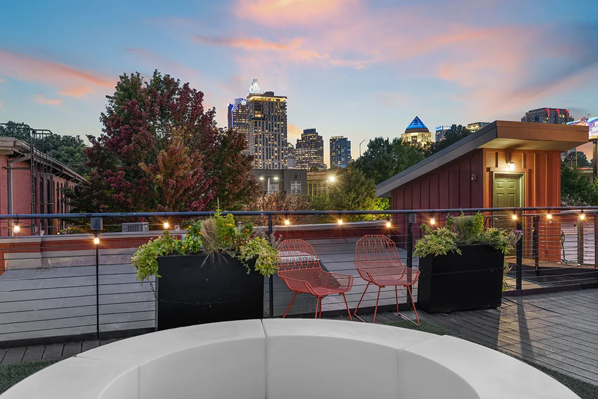 Charming rooftop patio with modern seating, lush planters, and stunning city skyline views at sunset at Alpha Mill Apartments in NODA Charlotte