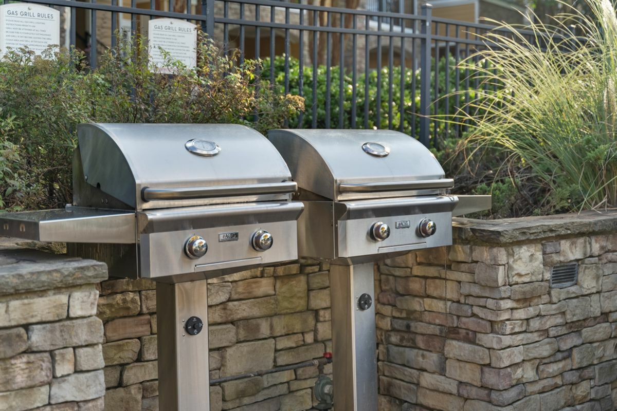 Modern outdoor grill area with sleek stainless steel BBQs and elegant stone wall backdrop, ideal for entertaining at Cottonwood Reserve Apartments in Charlotte