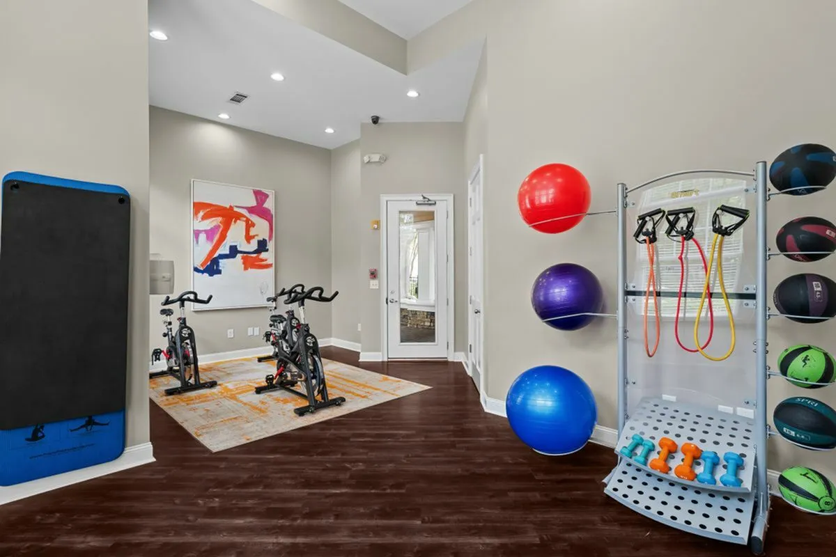 Modern spin and yoga studio with exercise bikes, vibrant stability balls, resistance bands, and dumbbells on sleek hardwood floors at Cottonwood Reserve in Charlotte, NC