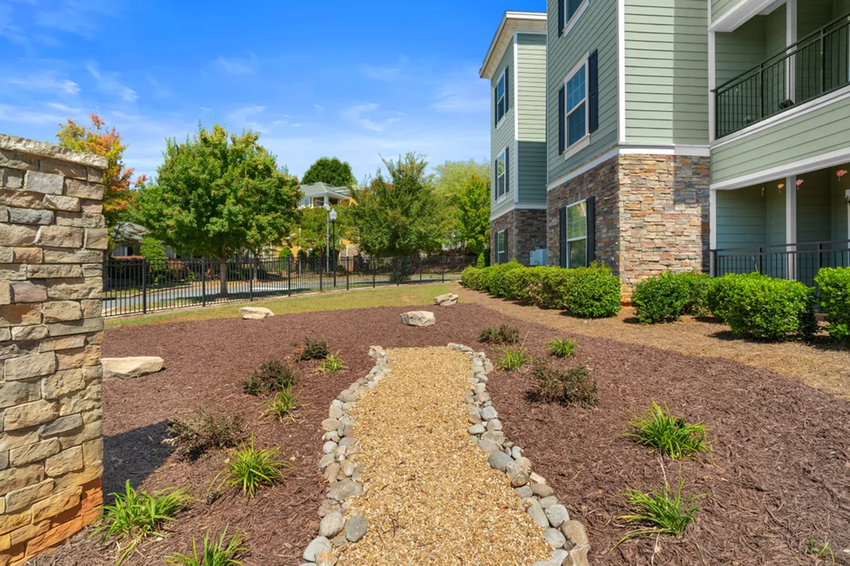 Charming modern apartment exterior with stone accents, lush greenery, and a scenic walkway under a clear blue sky Cottonwood Reserve in Charlotte, NC
