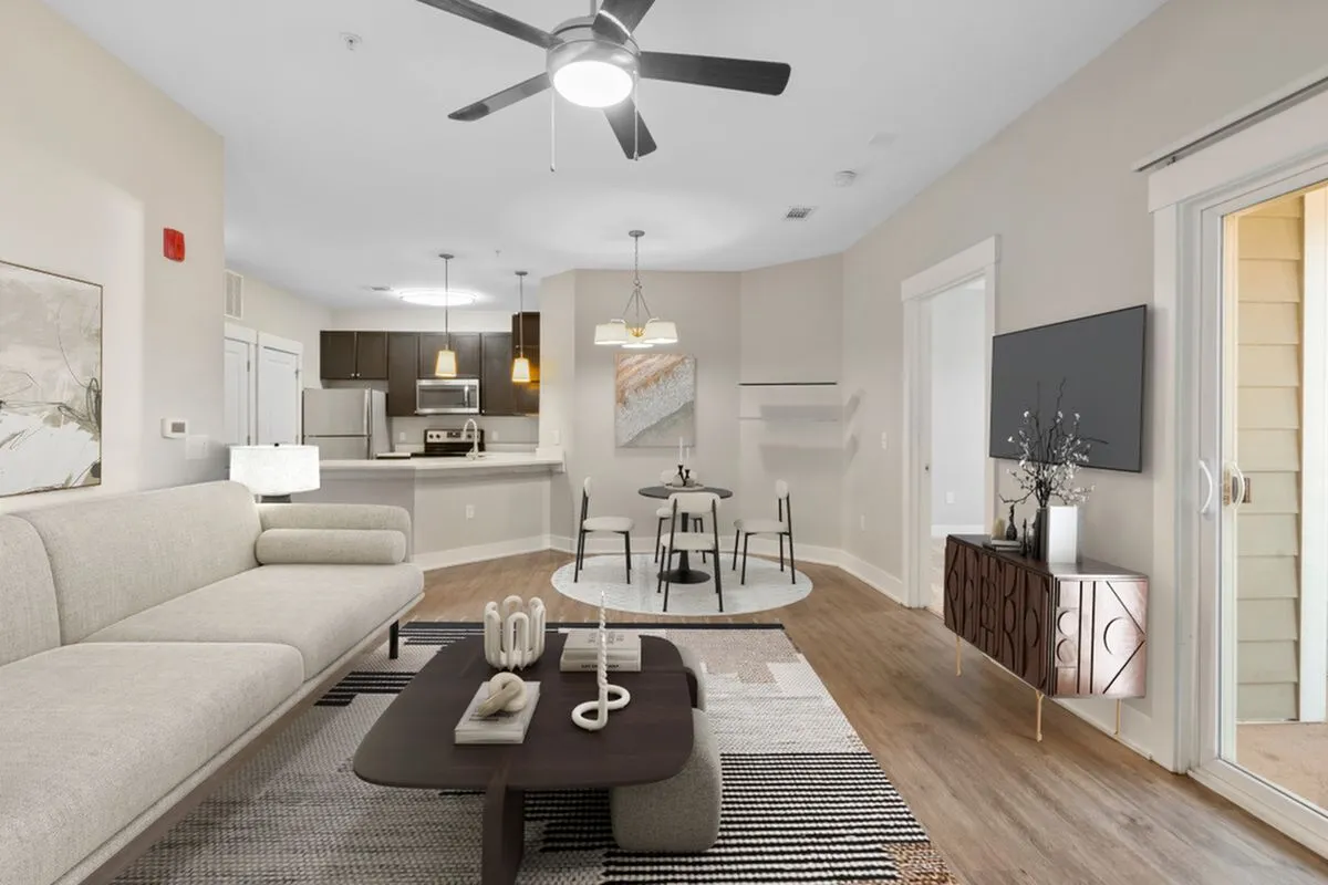 Contemporary open-plan living room with elegant furniture, modern kitchen with stainless steel appliances, and a cozy dining area, all enhanced by natural light and stylish decor at Cottonwood Reserve Apartments in Charlotte NC
