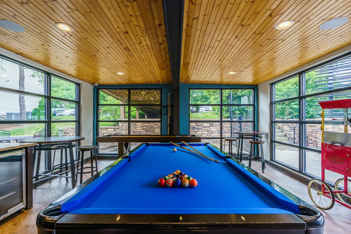 Bright and inviting recreational room featuring a sleek blue billiards table, ample natural light from large windows, and cozy seating areas.