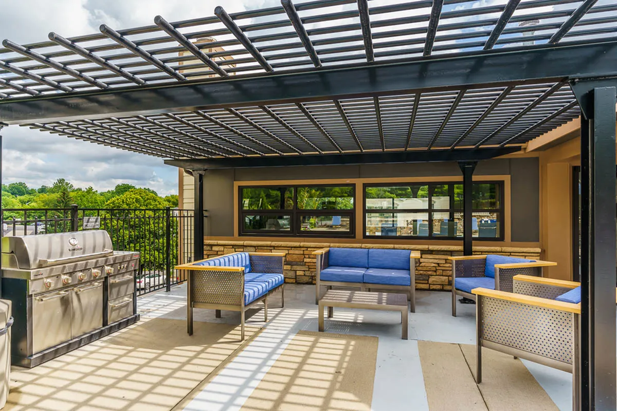 Chic rooftop terrace with modern blue seating and stainless steel grill under a stylish pergola, overlooking lush greenery.