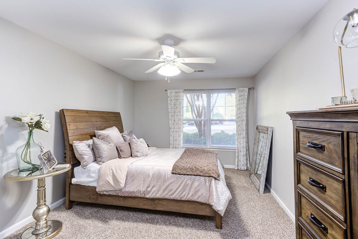 Inviting bedroom with a cozy wooden bed, plush pillows, elegant side table, and large window offering natural light.