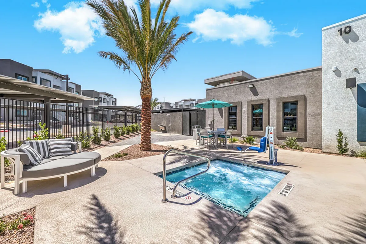 Luxurious apartment complex with a refreshing pool, modern outdoor seating, and a vibrant palm tree under a clear blue sky.
