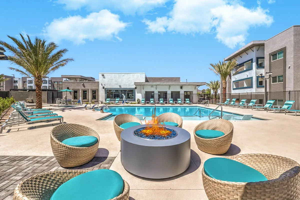 Luxurious apartment complex featuring a sparkling pool, modern fire pit, and stylish outdoor seating under clear blue skies.
