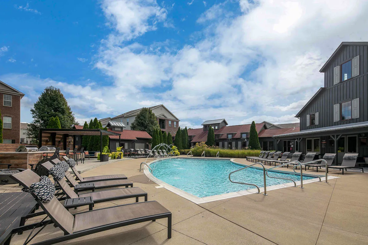 Charming apartment complex featuring a luxurious outdoor pool with sun loungers, landscaped gardens, and inviting lounge areas under a clear blue sky.