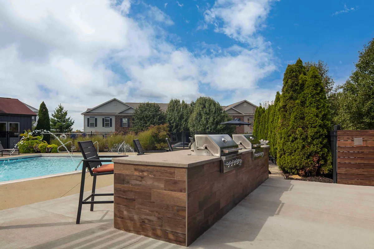 Charming outdoor space with a sleek pool, modern grill area, and lush greenery under a bright blue sky.