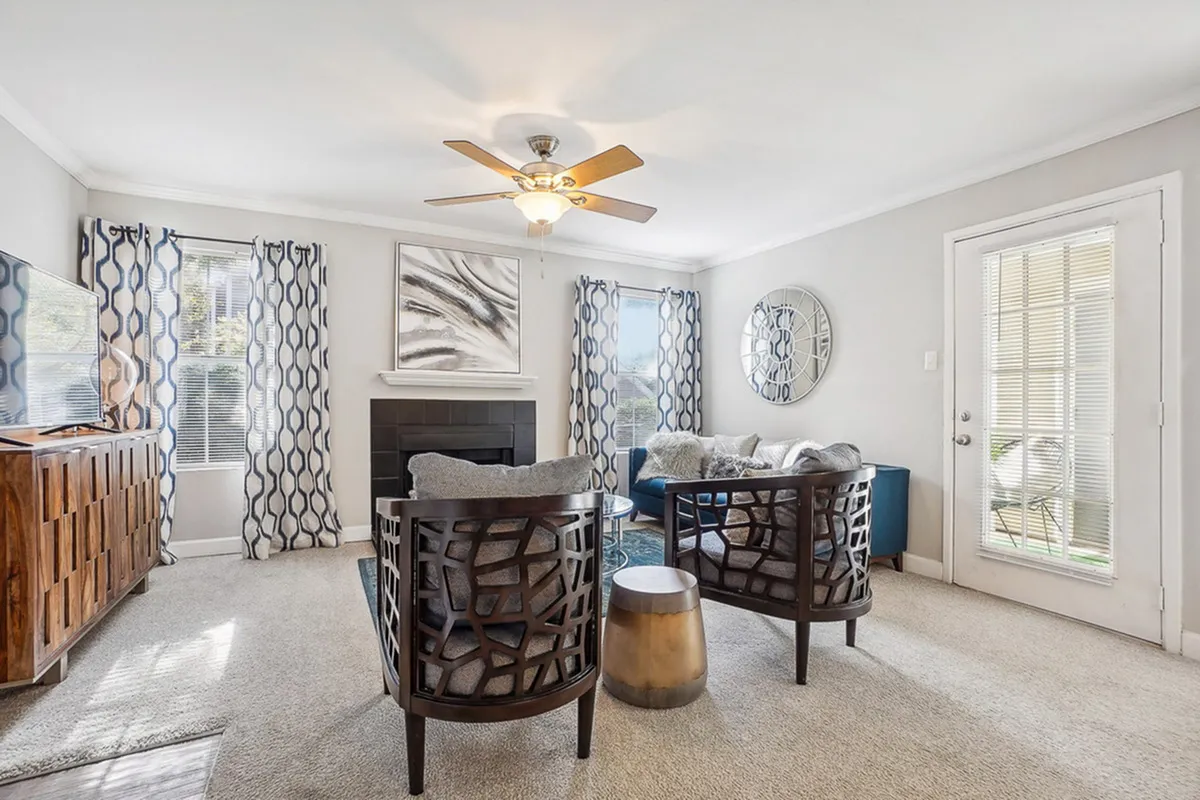 Elegant living room with modern decor, featuring stylish chairs, a cozy fireplace, and abundant natural light through large windows.