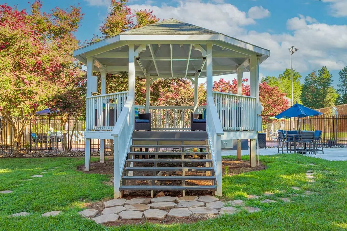 Charming white gazebo surrounded by lush greenery, perfect for outdoor gatherings in a serene setting.
