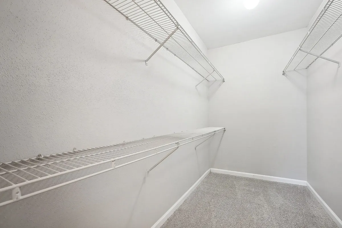 Spacious walk-in closet with sleek wire shelving and plush carpeting, offering ample storage solutions.