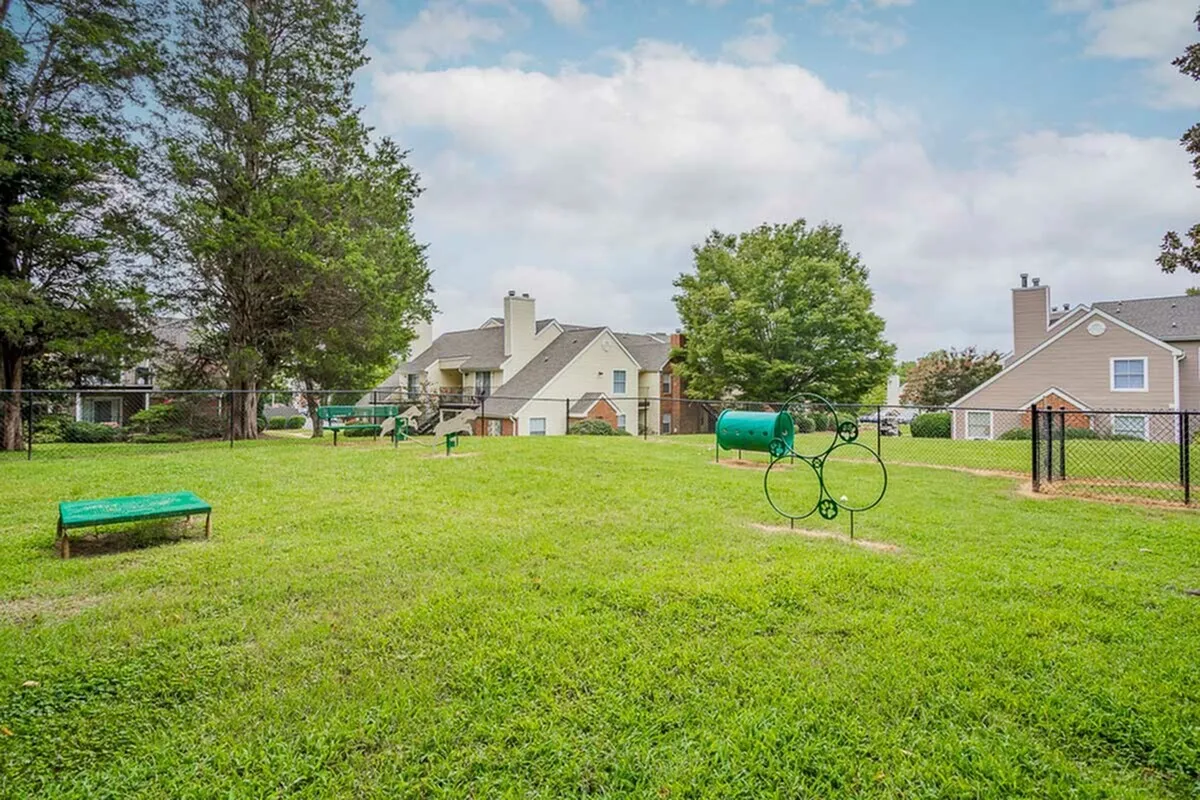 Serene apartment complex surrounded by lush greenery, featuring a well-maintained dog park with agility equipment.
