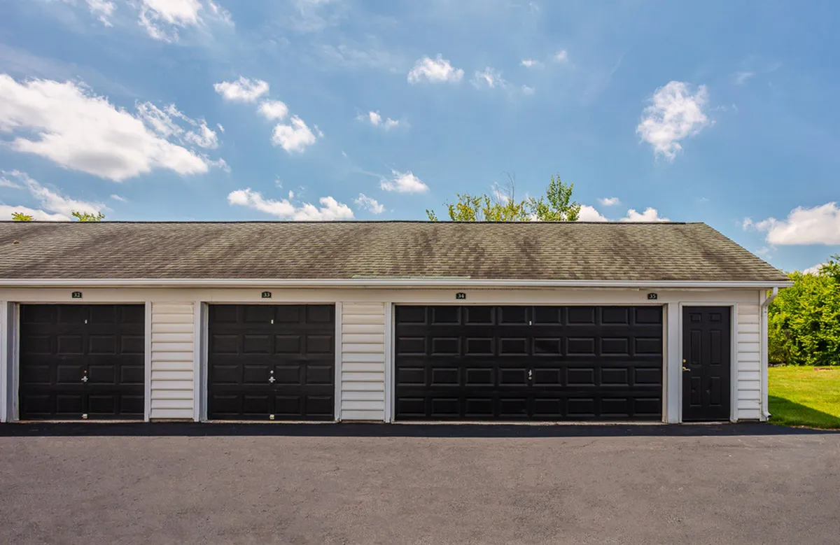 Charming white garage with multiple black doors under a clear blue sky, nestled in a serene neighborhood setting.