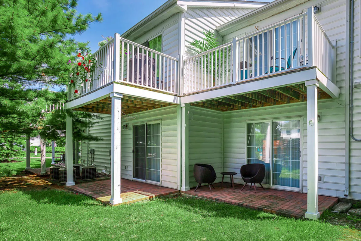 Charming apartment exterior with private balconies, lush green surroundings, and inviting outdoor seating areas.