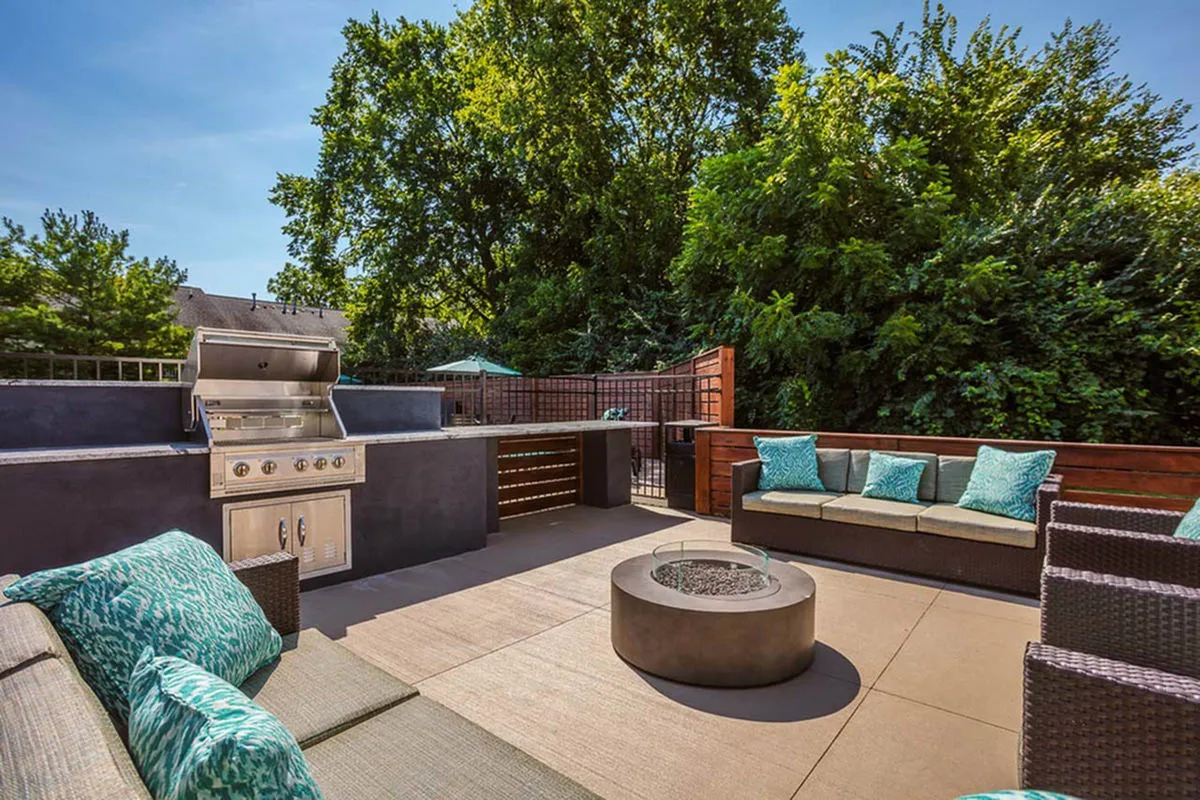 Chic outdoor patio featuring a modern grill station, comfortable seating with turquoise cushions, and a sleek fire pit surrounded by lush greenery.