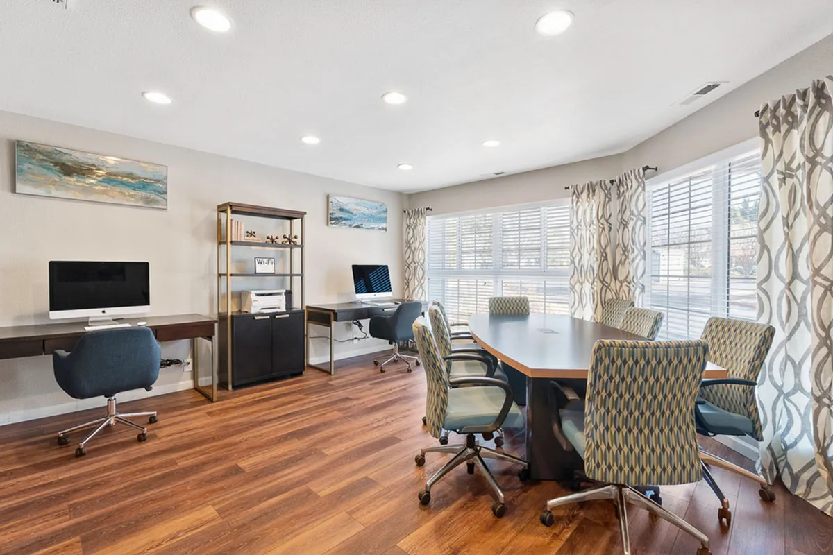 Modern office space with elegant wooden floors, natural light from large windows, and stylish decor, featuring a conference table surrounded by patterned chairs and equipped workstations at Antero Apartments in Colorado Springs