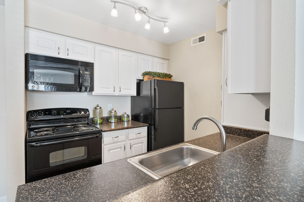 Modern kitchen with sleek black appliances, elegant white cabinetry, and a stylish granite countertop at Antero Apartments in Colorado Springs