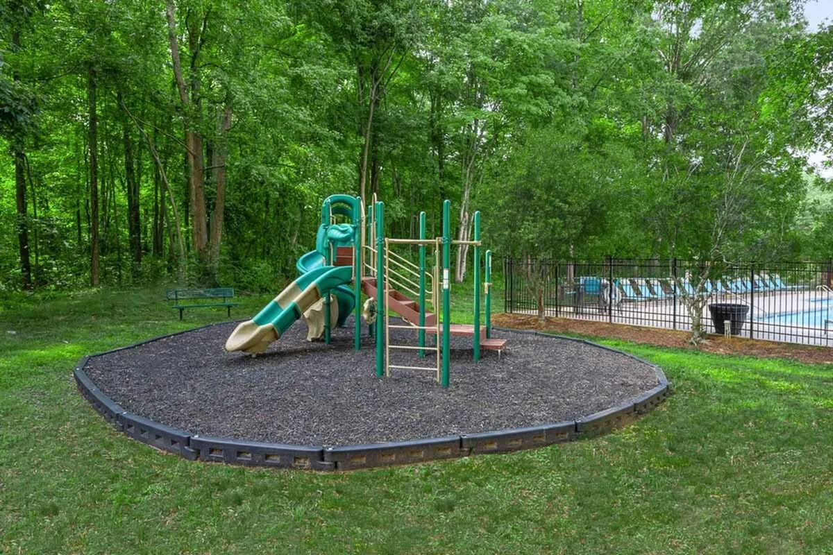 Charming playground area with vibrant slides and climbing structures surrounded by lush greenery, adjacent to a serene swimming pool, ideal for family recreation.
