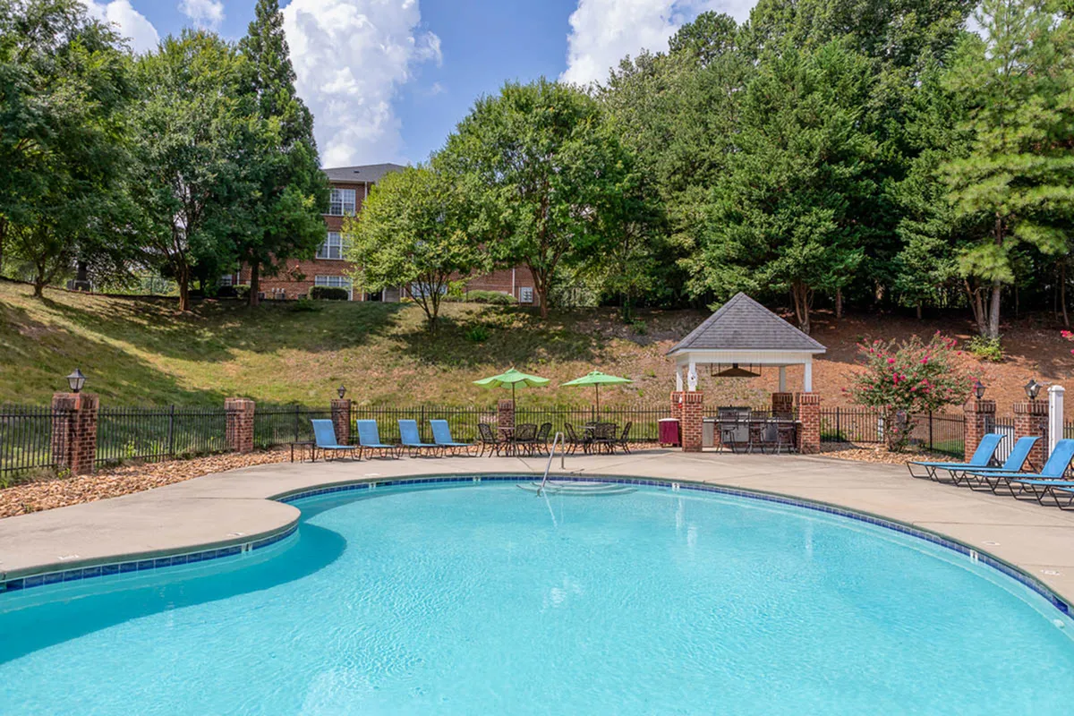 Inviting outdoor pool area with comfortable lounge chairs, shaded seating, and lush greenery in a serene residential community.