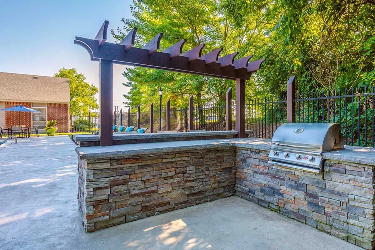 Charming outdoor kitchen with stone barbecue area under a stylish pergola, surrounded by lush greenery and a cozy seating area.