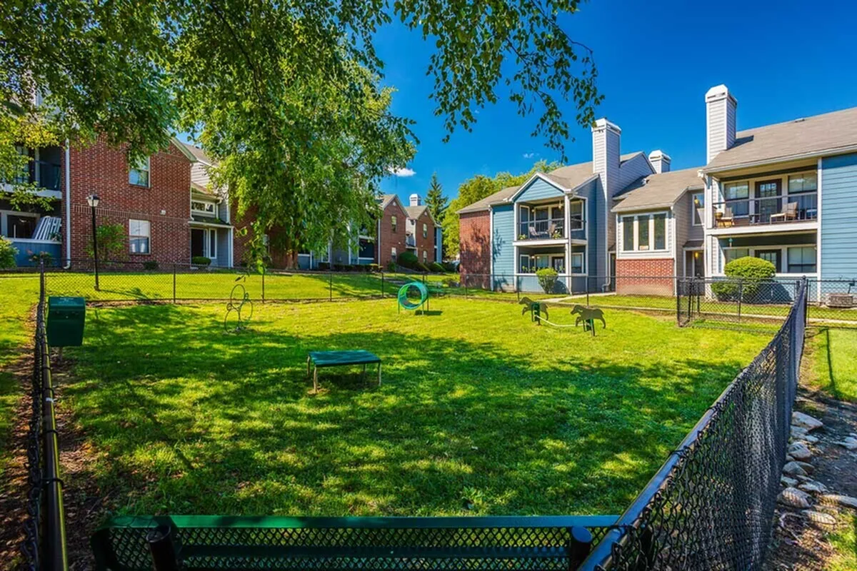 Charming apartment complex with lush green courtyard, pet-friendly amenities, and modern architecture under a vibrant blue sky.