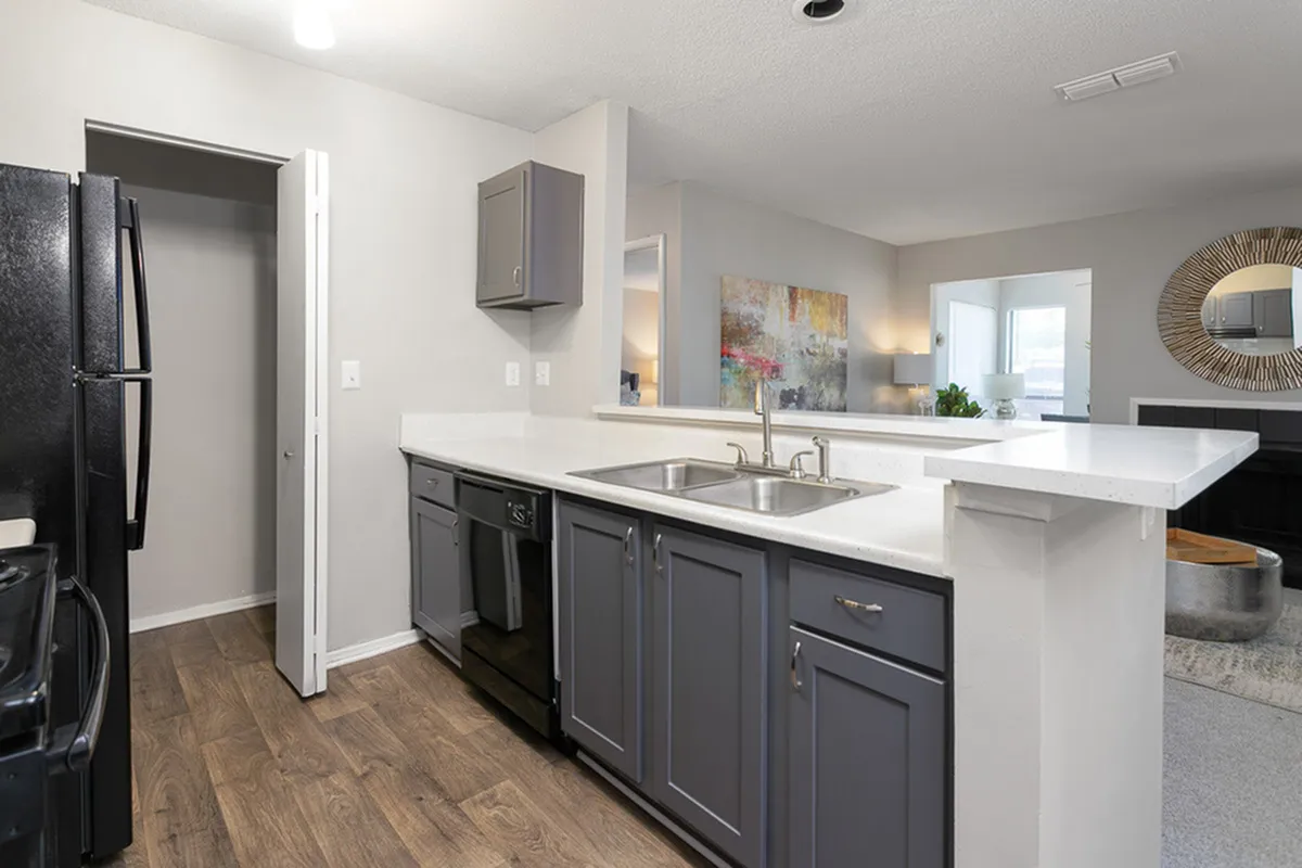 Modern kitchen with elegant dark cabinets, sleek white countertops, and wood flooring, seamlessly leading to a cozy living area with stylish decor.